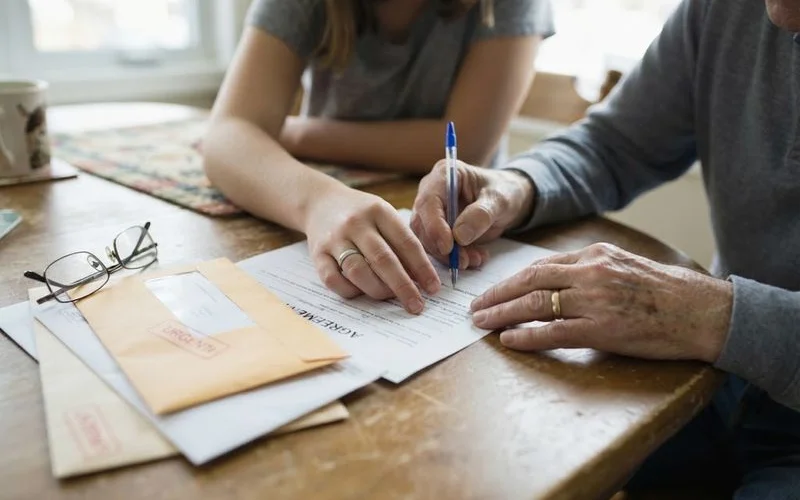 An adult child sitting with an aging parent reviewing mortgage paperwork together at a kitchen table
